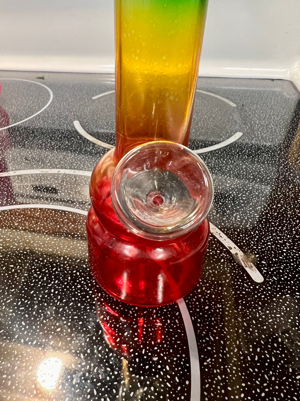 Ripkitty 5-inch soft glass water pipe, rasta red-yellow-green gradient, close-up of base and bowl joint, black stovetop background