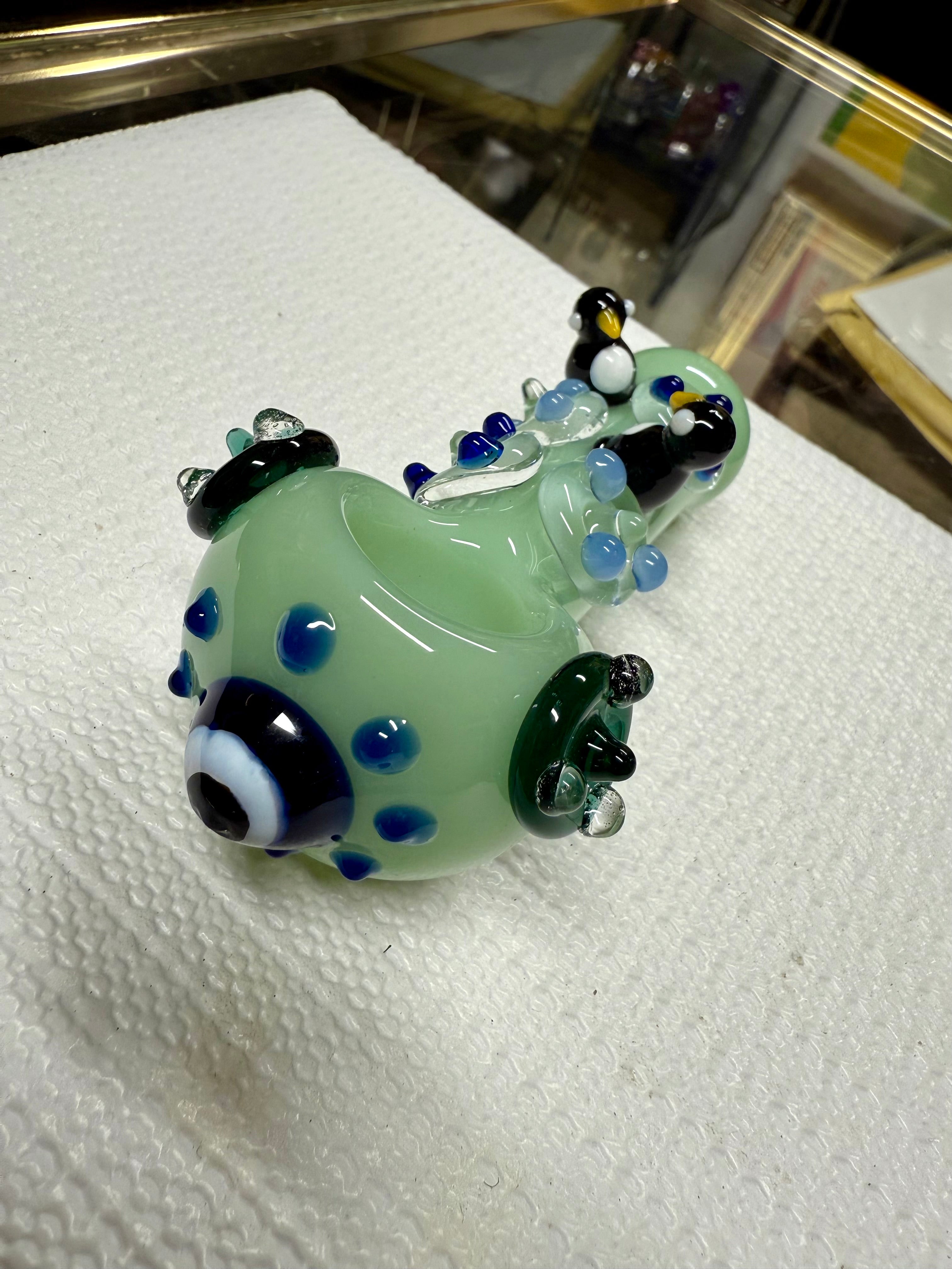 Ripkitty penguin art spoon pipe in mint green — sculpted penguin figures on top, blue dot pattern, dark green flipper accents, white background