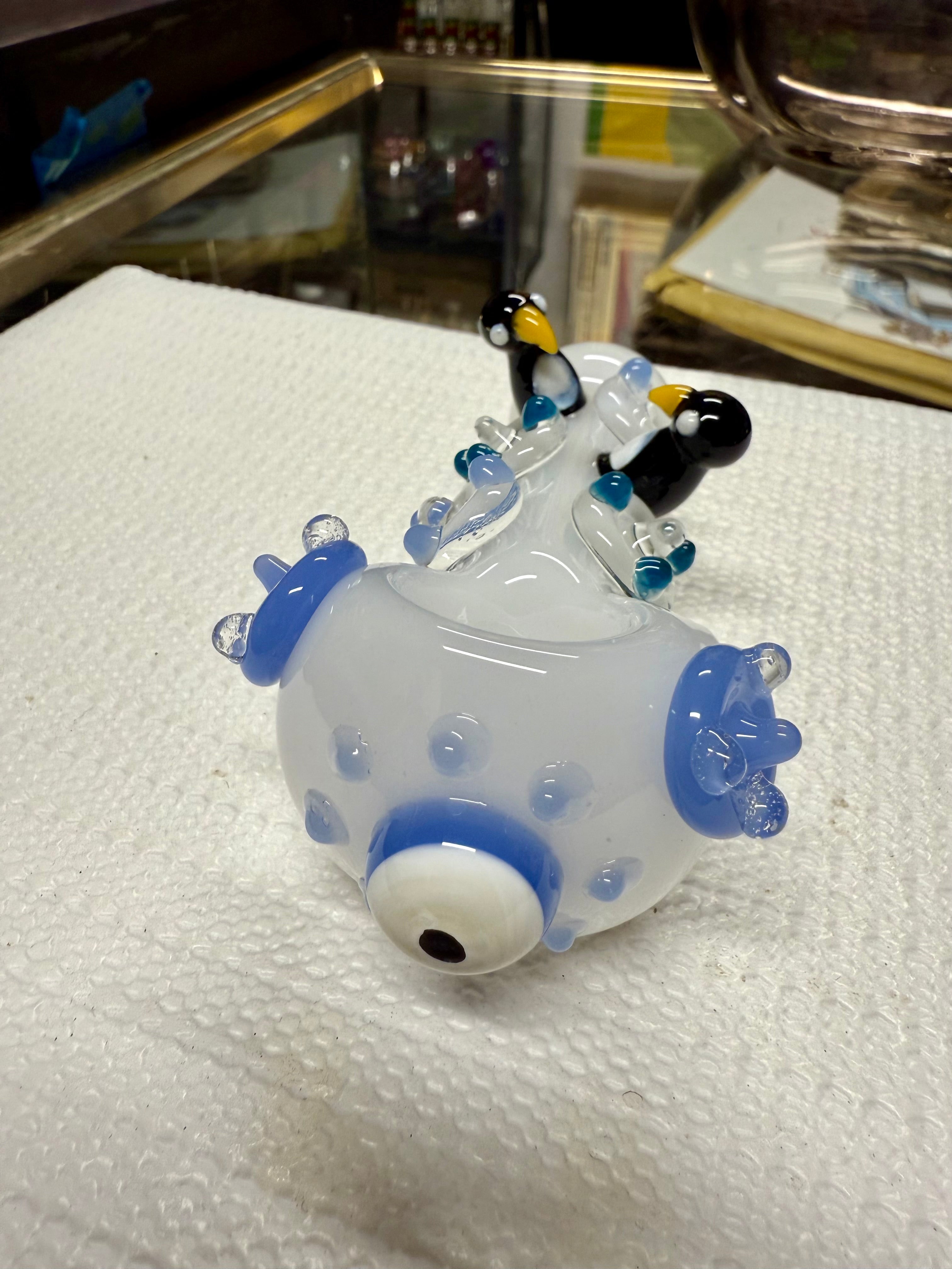 Close-up of Ripkitty penguin art pipe bowl — evil eye glass accent with blue ring on periwinkle body, penguin sculpts in background