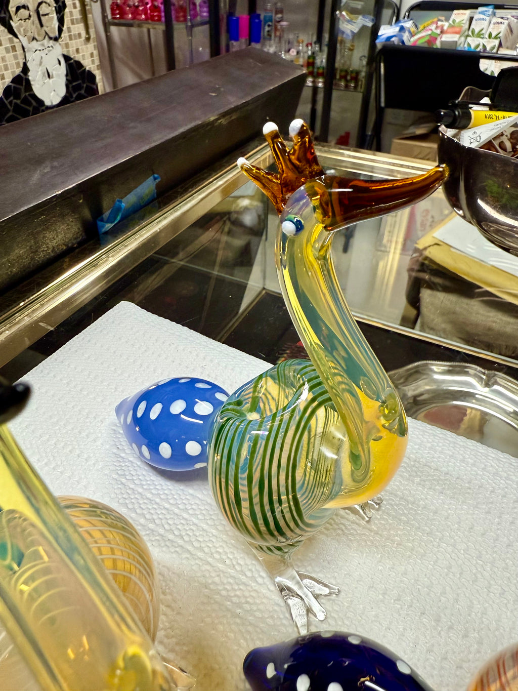  Ripkitty 5" peacock glass pipe — three-quarter front view showing peacock neck, glass eye bead, teal-striped body, and blue dot bowl